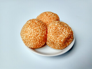Three fried sesame balls with mung beans filling, called onde-onde in Indonesia, placed in a white small plate.