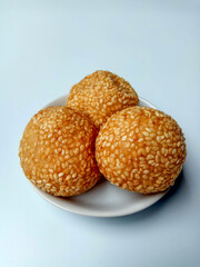 Three fried sesame balls with mung beans filling, called onde-onde in Indonesia, placed in a white small plate.