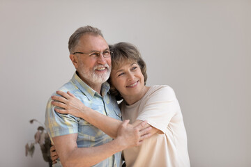 Cheerful dreamy older 60s married couple hugging with love, care, tenderness, looking away with goof thoughts, thinking on future plans, dreaming on happy retirement. Elderly age relationship concept