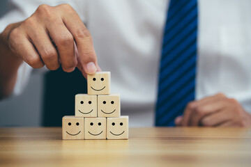 Closeup hands holding smiley face icon on wooden cube, service rating, leadership and corporate...