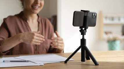 Focus on cellphone standing on table on tripod stabilizer, motivated indian young female blogger...