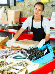 Smiling female fishmonger offering fresh fish and seafoods for sale in shop