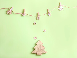 Five handmade wooden snowflakes on the rope with the pegs on the green background and place for your text. Christmas or New Year beige and green banner.