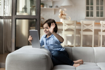 Little boy sit on sofa at home wave hand greeting friend, start videocall conversation through...