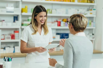 Wall murals Pharmacy Female pharmacist selling medications at drugstore to a senior woman customer