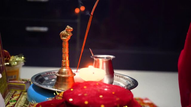Hands of indian mother daughter conducting puja rituals using a red tie and dye saree with gold gota border with a small earthenware diya lamp burning oil with a golden bell