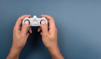 Hand holding and using silver retro style radio remote control for a toy isolated on blue background with copy space. Game controller  joystick, flat lay, minimal style.