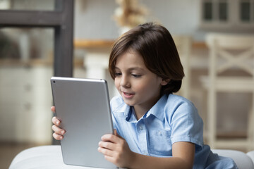 Close up lovely little boy relaxing at home alone with wireless digital tablet device. Parental control software apps, children safe usage of modern tech, cyberspace, internet, fun and leisure concept