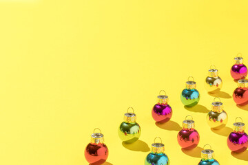 Creative pattern made with colorful Christmas baubles. Minimal yellow New Year party background.