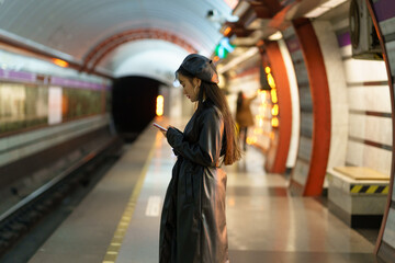 Korean girl with smartphone at empty metro platform. Stylish asian female browsing social media...