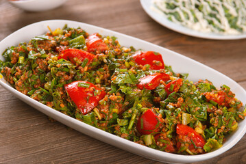 Tabbouleh salad with bulgur, tomatoes, parsley and green onion in plate on wooden table. Traditional middle eastern or arab dish.