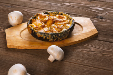 Homemade julienne with cheese and mushrooms . A hot dish with baked cheese crust on a wooden  table.
