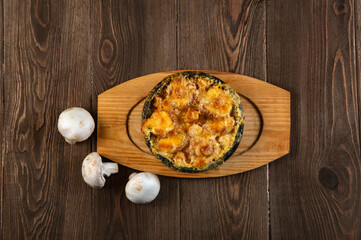 Julienne in a pot and mushrooms  on a wooden  table. Mushrooms baked with cheese crust in pan  .top view