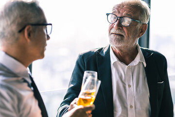 Picture of young business man talking to his older business partner. They are in white shirt and black tie. They are sitting on a table in a hotel lobby. 