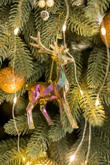 Close up of holidays location with gold ball and glass deer toys and garlands on green Christmas tree