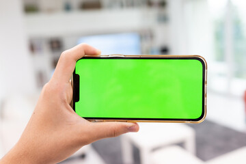 Hand in modern living room via smart home on mobile phone with blank green screen. High quality...