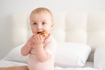 baby girl in light pink bodysuit nibbling wooden toys on white bedding on bed
