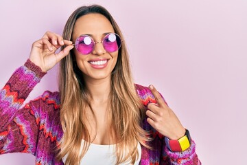 Beautiful hispanic woman wearing bohemian and hippie style with pink sunglasses smiling happy pointing with hand and finger