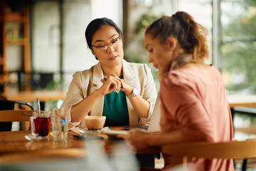 Asian entrepreneur and her female colleague having business meeting in a cafe.