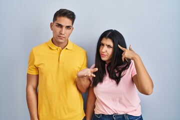 Naklejka premium Young couple standing over isolated background confused and annoyed with open palm showing copy space and pointing finger to forehead. think about it.