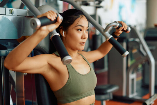 Asian female athlete doing weight exercises for upper body strength during sports training in a gym.