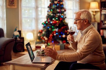 Senior man drinks glass of wine while talking to his son via video call on Christmas.