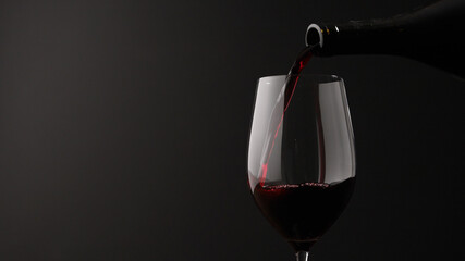 Naklejka na ściany i meble pour red wine into wineglass on black background