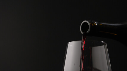 pour red wine into wineglass on black background