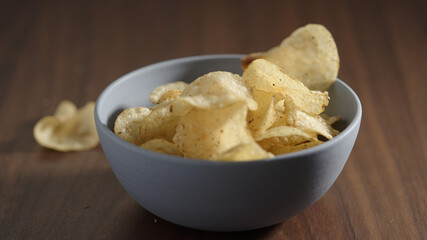 potato chips with black pepper falling into blue bowl on wood table