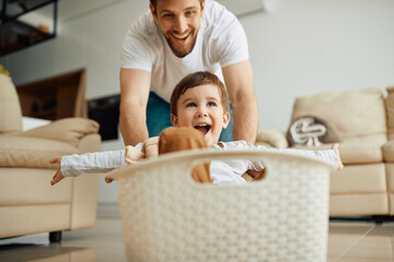 Happy kid with arms outstretched has fun while being pushed in laundry basket by his father.