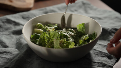 man mixing dressing over romaine leaves in white bowl