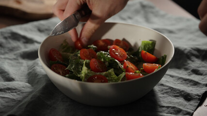 man add cherry tomatoes to romaine leaves in white bowl