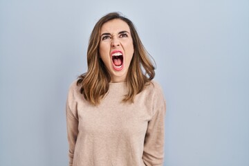 Young woman standing over isolated background angry and mad screaming frustrated and furious,...