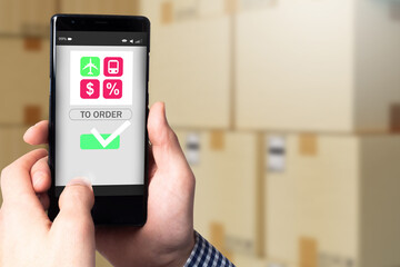 Ordering goods via phone. Concept - shopping in online store with delivery. Logistics options symbols in phone. Hands with application on background of cardboard boxes. Remote ordering of goods.