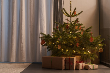 Small christmas tree with gifts in paper wrap near window in the evening