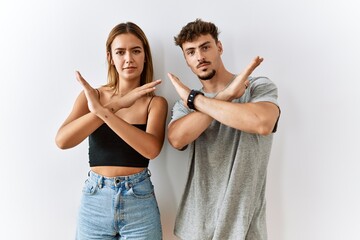 Young beautiful couple standing together over isolated background rejection expression crossing arms doing negative sign, angry face