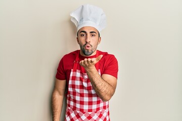 Young hispanic man wearing baker uniform looking at the camera blowing a kiss with hand on air being lovely and sexy. love expression.