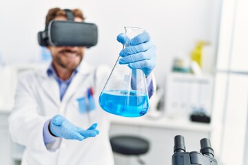 Middle age hispanic man wearing scientist uniform using vr glasses holding test tube at laboratory
