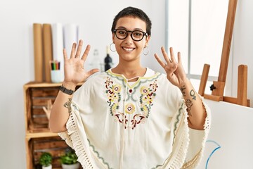Young hispanic woman with short hair at art studio showing and pointing up with fingers number nine...