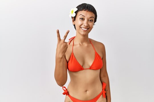 Young hispanic woman with short hair wearing bikini showing and pointing up with fingers number two while smiling confident and happy.