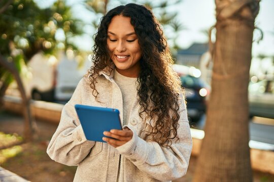 Young latin woman smiling happy using touchpad at the city.