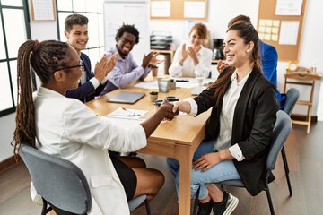 Group of business workers smiling and clapping to partners handshake at the office.