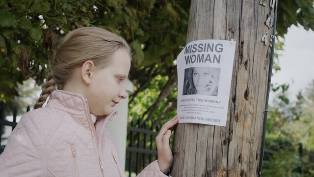A sad, crying child stands at an ad for a missing woman.