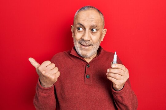 Handsome mature man holding spark plug pointing thumb up to the side smiling happy with open mouth