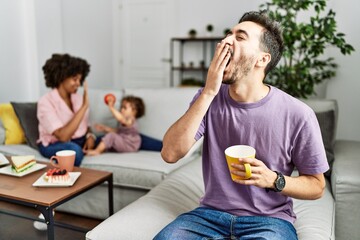 Hispanic father of interracial family drinking a cup coffee bored yawning tired covering mouth with hand. restless and sleepiness. - obrazy, fototapety, plakaty