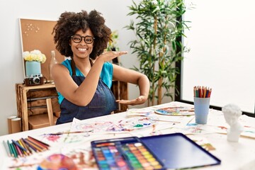 Beautiful african american woman with afro hair painting at art studio gesturing with hands showing big and large size sign, measure symbol. smiling looking at the camera. measuring concept.