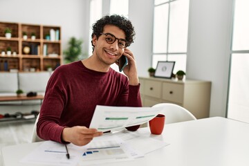 Young hispanic man talking on the smartphone working at home.