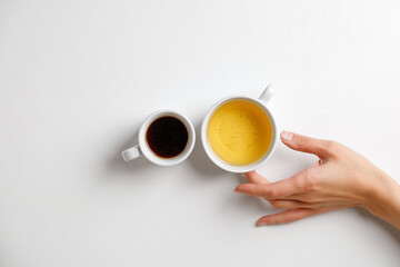 Coffee opposite tea. Mug of black coffee opposite mug of green tea on a white table with hand. Minimalism.
