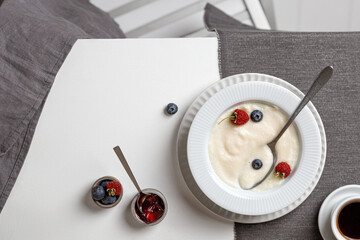 a plate of semolina porridge and berries on a white table and a gray napkin with coffee. Top view