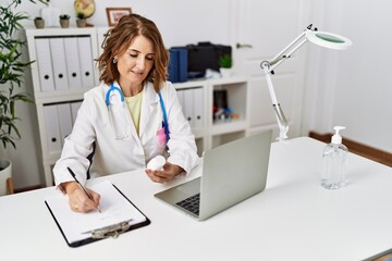 Middle age hispanic woman wearing doctor uniform holding pills at clinic